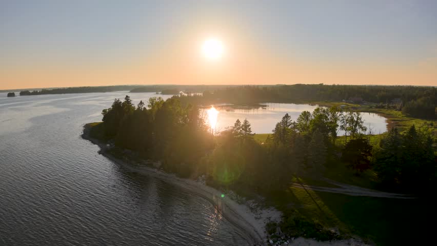 Aerial drone footage of a golden sunset casting warm light over forested islands and calm waters in the Les Cheneaux Islands, Upper Peninsula, Michigan.