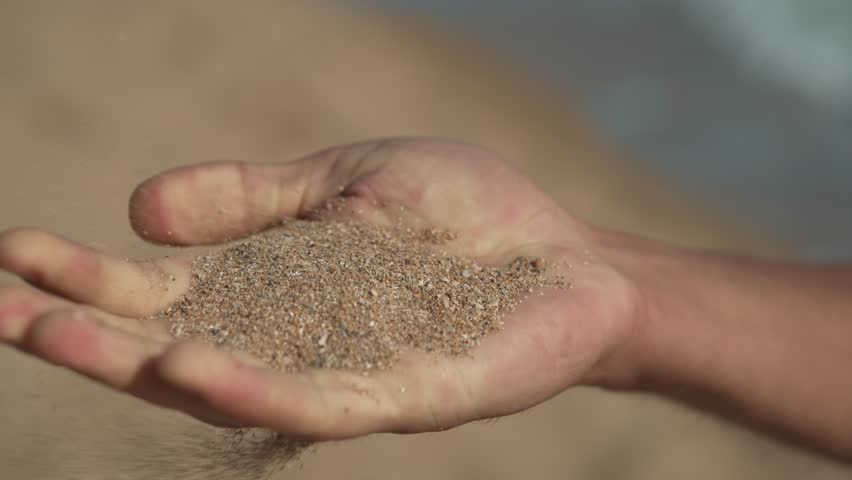 Sand Blown by Wind Through Male Hand at Sunset
