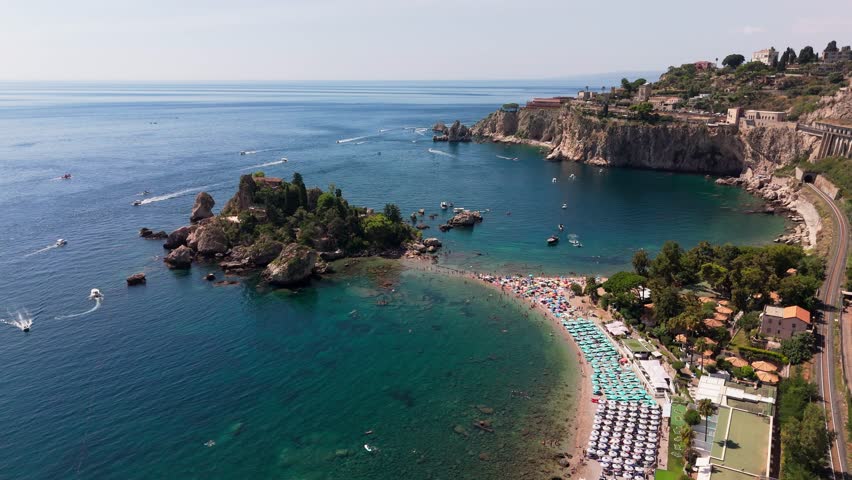 Drone pans left to right around Isola Bella, showcasing the island with vast Mediterranean waters and sparkling coastline.