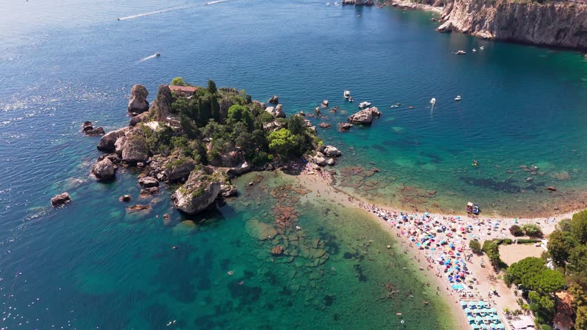 Drone pans left to right around Isola Bella, highlighting the narrow strip linking the island to the mainland and surrounding coastal scenery.