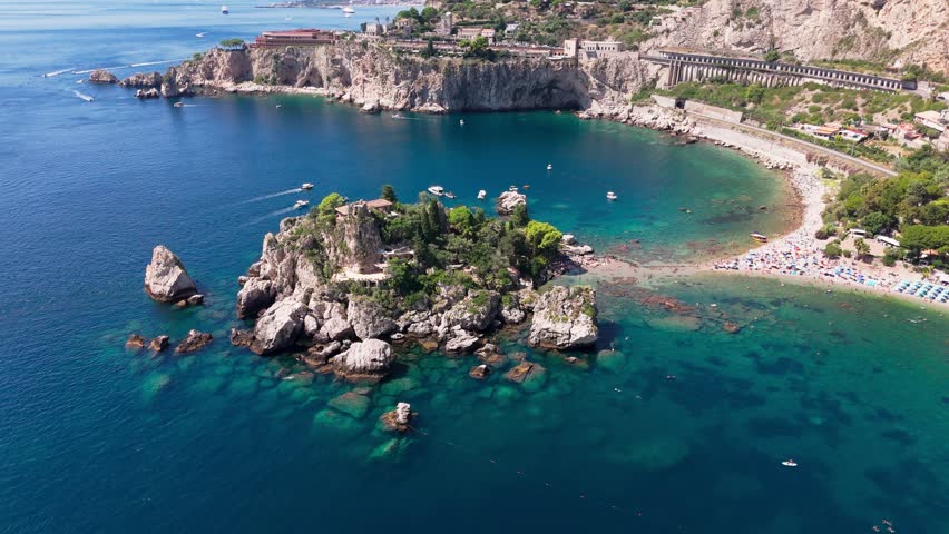 Drone orbits closer from right to left, highlighting Isola Bella, the beach, and detailed coastal features with clear water and rocks.