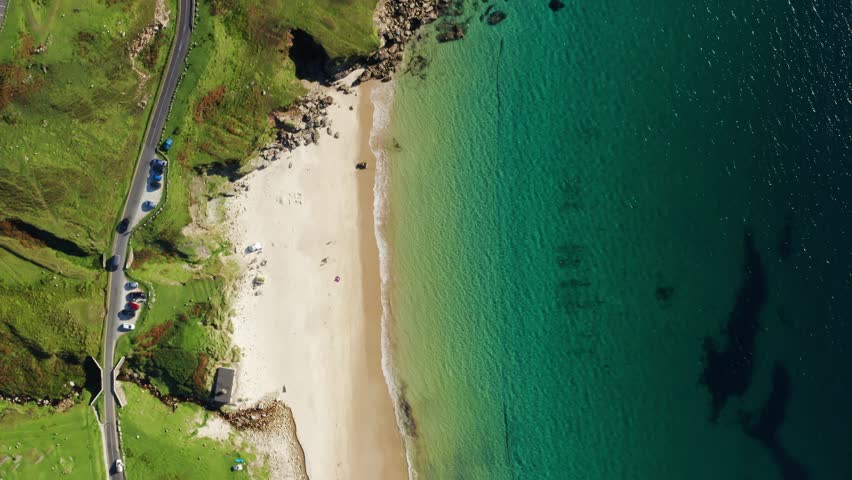 Aerial top down flight over Keem Beach coastal road with rugged cliffs and cars driving on Achill Island