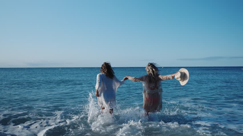 Women holding hands and playing in ocean waves, slow motion