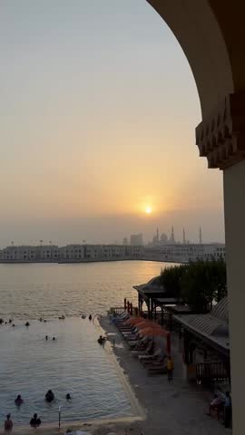Beautiful orange sunset over calm ocean waves with people enjoying by the pool