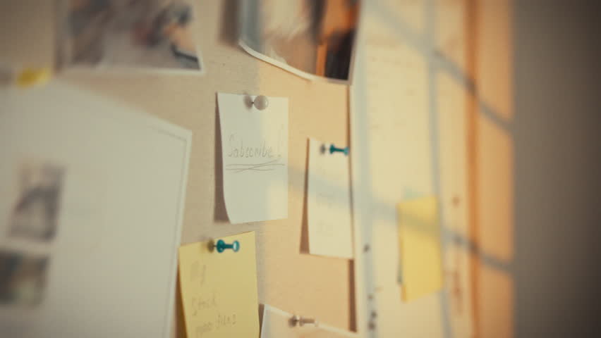 A hand points to various photos and notes pinned on a bulletin board. The individual is likely organizing thoughts or memories in a creative workspace. Natural light illuminates the area