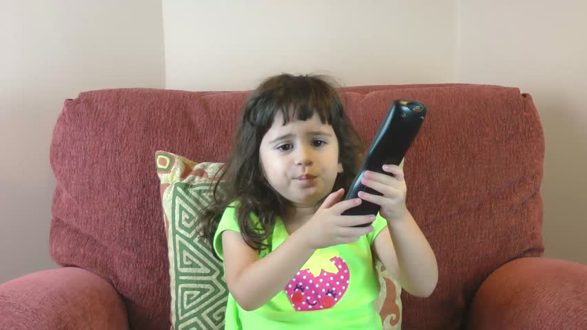 Frustrated little girl with tv remote trying to change the channels