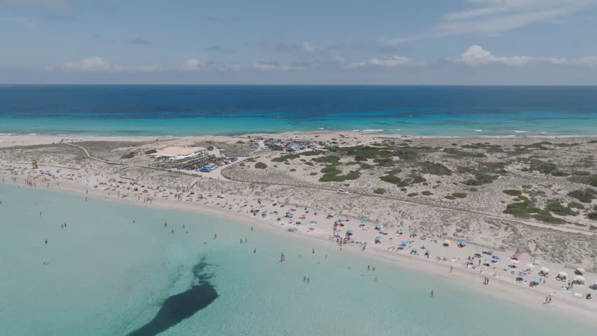Low drone pullback from anchored boats in the clear turquoise waters of Ses Illetes, revealing the sandbanks and shallow shoreline of Formentera.