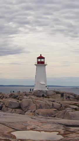 Vertical Video, Time-Lapse Visitors Walk Swiftly Over The Large Granite Cliffs Around The Lighthouse. Atlantic Ocean Shimmers In Background This Iconic Nova Scotia Location. Popular Scenic Destination