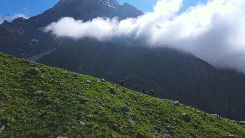 Slow drone approach across alpine meadow to the huge Mizhirgi icefall in Bezengi, Caucasus. Clear summer weather, rugged cliffs and moving cloud create cinematic landscape for travel content