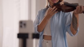Young female musician performing violin during virtual online concert, streaming music content through smartphone while creating engaging performance for social media followers - Powered by Shutterstock - Get 15% off with code: PIKWIZARD15