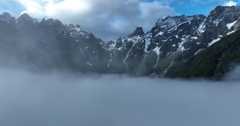 Aerial footage of beautiful high altitude snow capped mountains in the fog landscape