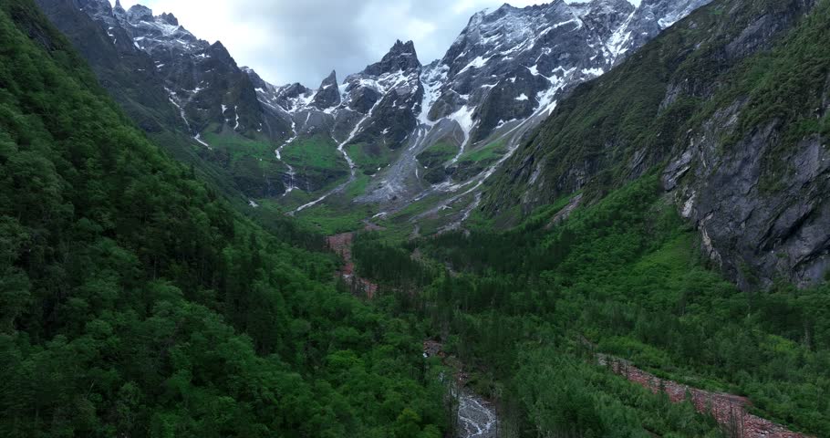 Aerial footage of beautiful high altitude green forest  and red stone in the valley under snow capped mountain andscape