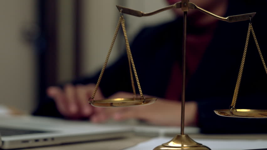Close-up of golden balance scales symbolizing justice with a lawyer working in the background at a law office. Ideal for legal, law firm, or justice concept.