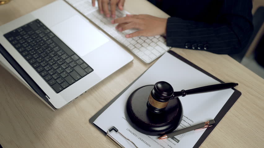 Lawyer hands typing on keyboard next to laptop, gavel, and legal contract, representing legal work, law firm, and corporate justice in digital age.