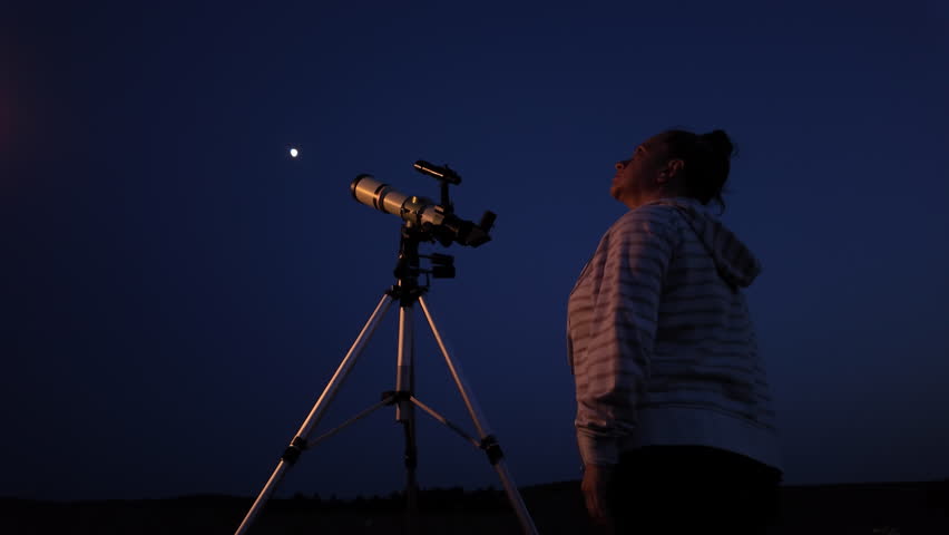 Amateur astronomer using telescope for watching stars, Moon, planets and other celestial objects from a field in nature.