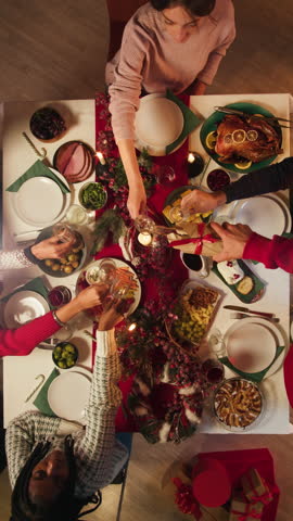 Friends giving presents to each other top view, celebrating new year, sitting at dining table. International young people making surprises. Diverse students during christmas party at home. 