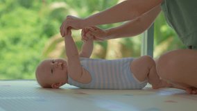 Mother practices gentle baby gymnastics with her 3-month-old son near a large window overlooking lush green trees, promoting bonding and early physical development. Slowmotion video. - Powered by Shutterstock - Get 15% off with code: PIKWIZARD15