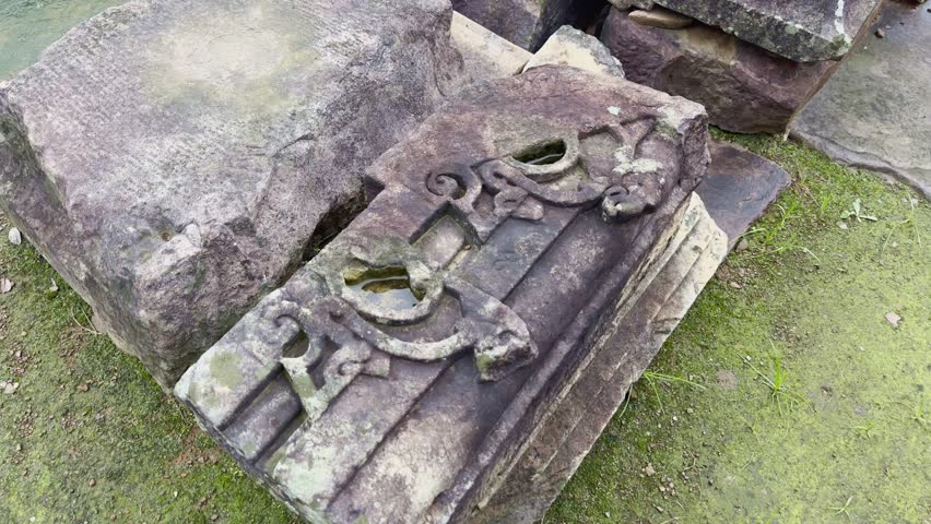 A static shot of a weathered stone block featuring faint ornamental carvings. Its moss-stained surface and worn edges speak of centuries of history, artistry, and natural erosion.