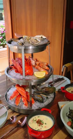Luxury seafood platter on ice in restaurant setting features oysters, lobsters, shrimp, mussels. Fresh delicacies arranged for gourmet dining experience. Vertical
