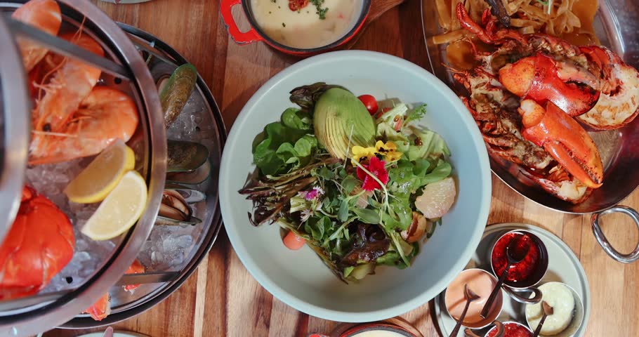 Gourmet seafood platter, vibrant salad, creamy sauces on wooden table, showcasing fresh lobster, shrimp, avocado in restaurant setting, ideal for culinary or dining themes.