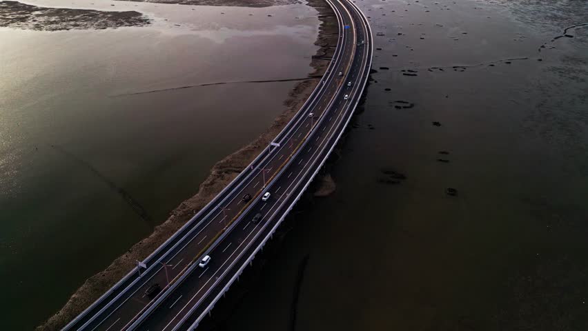 From above Bali Mandara Toll road curves across wide tidal mudflats revealed at low tide the drone footage highlights tropical coastal patterns and the strong design of the island bridge