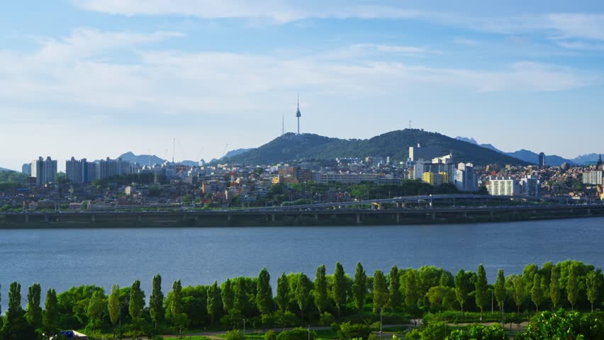 Iconic Seoul cityscape featuring Namsan Tower, the lush Hangang Park, and traffic on the Gangbyeongbuk-ro expressway - Beautiful static aerial view