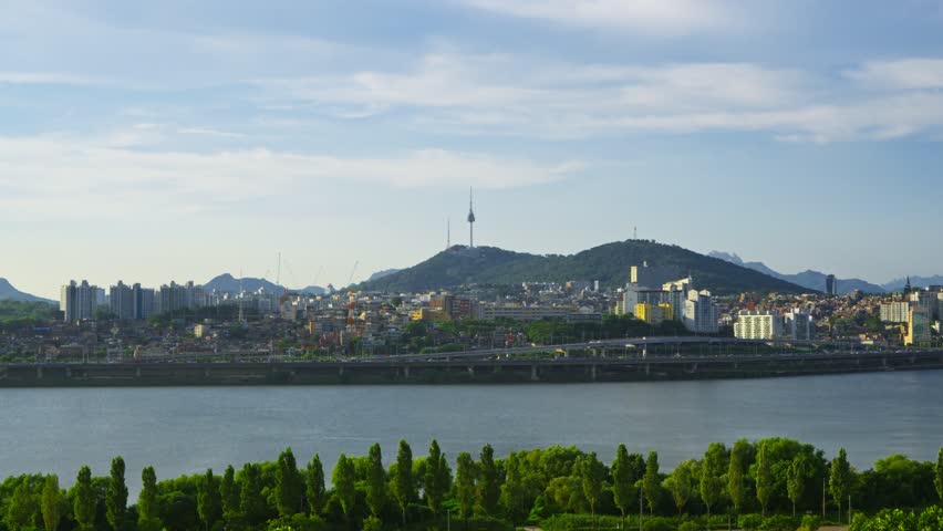 Bright cityscape shows iconic N Seoul Tower atop lush Namsan mountain overlooking Han River and modern buildings on clear day