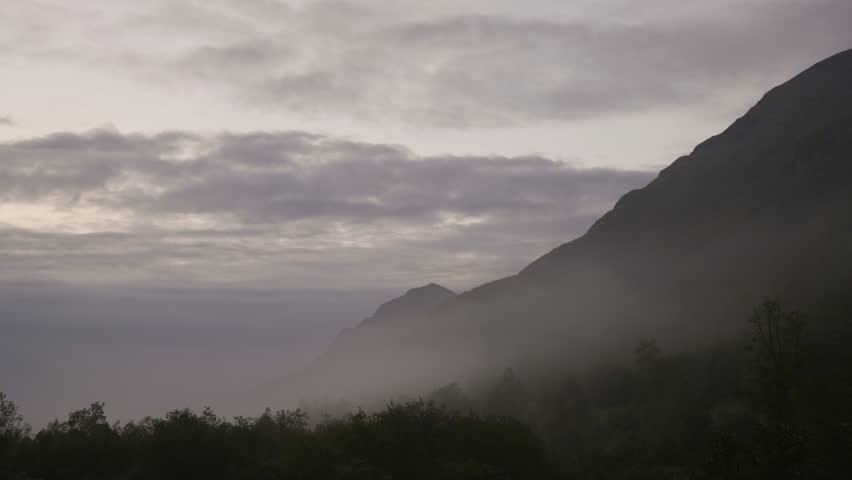 Fog lays low on the mountainside with the sunset hitting the moutains range in Sunnmøre, Norway