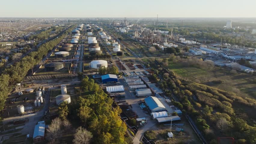 Drone footage of oil and gas refinery with storage tanks and processing facilities in Argentina at sunset.