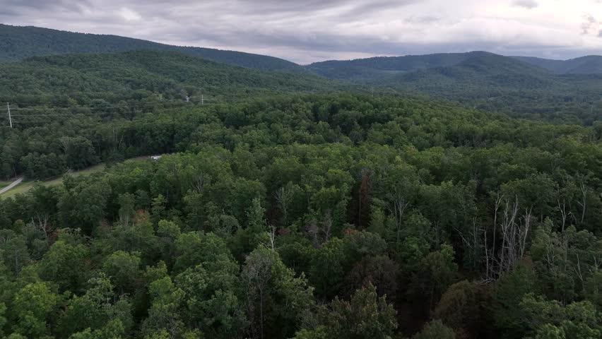 Aerial panorama of forest landscape and hills under grey dark cloudy sky in USA. Wide shot. Blue ridge mountains of Virginia in distance.