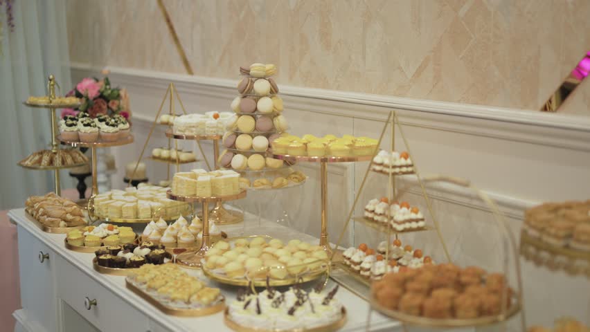 Lavish dessert buffet showcasing a colorful assortment of cakes, pastries, cupcakes, macarons, and tarts arranged on elegant golden stands