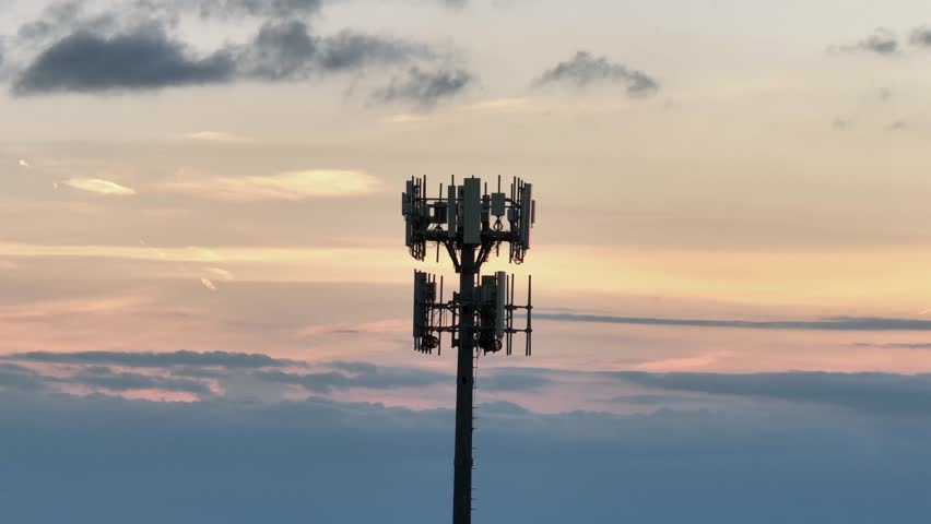 Silhouette of cell tower over cloudscapes and sunset light. Aerial orbit shot. Telecommunication tower or radio mast in America.