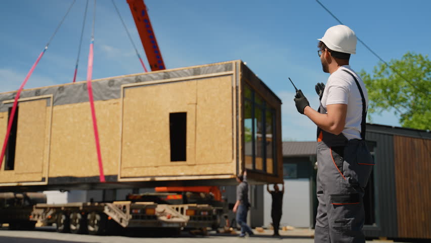 Construction worker directing crane lifting prefabricated modular house