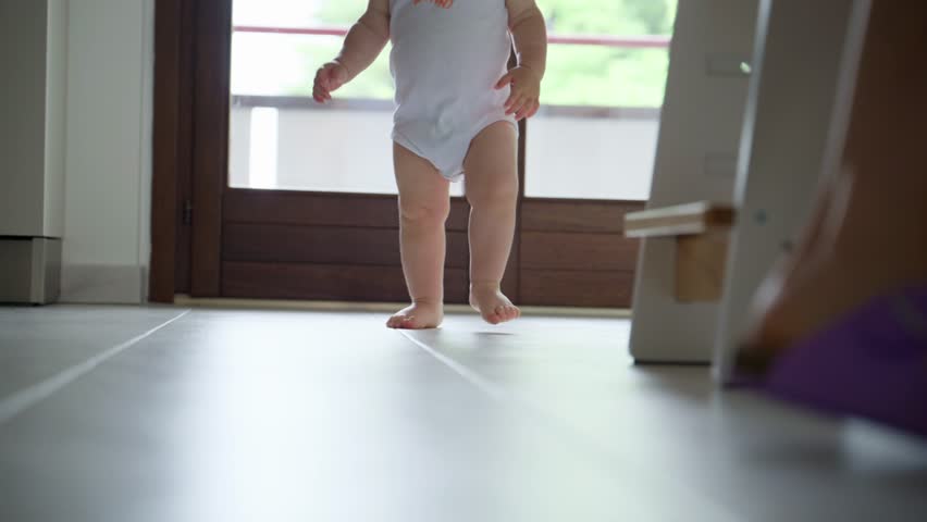 Low angle close-up of a baby's bare feet walking on a clean tile floor, emphasizing the movement and early stages of childhood mobility and development