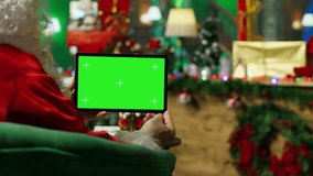 Santa Claus reads letters from kids on isolated screen device in Christmas ornaments adorn workshop. Old costumed man in holiday season ambiance holding chroma key tablet, camera A - Powered by Shutterstock - Get 15% off with code: PIKWIZARD15