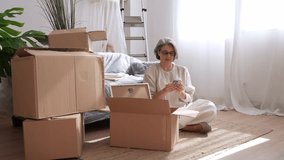 Senior woman carefully unpacking moving boxes, navigating smartphone while settling into bright, comfortable new apartment during relocation process - Powered by Shutterstock - Get 15% off with code: PIKWIZARD15