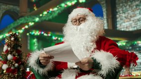 Santa Claus reading letters from kids after adorning workshop with Christmas ornaments. Elderly costumed man in holiday season ambiance reading children wish lists, camera A - Powered by Shutterstock - Get 15% off with code: PIKWIZARD15