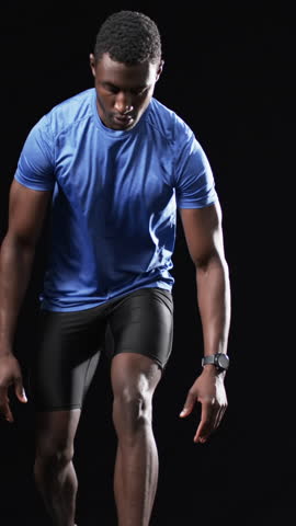 Vertical video: African American man lowering into sprint stance in studio with wristwatch. Athlete, sportswear, dynamic pose, motion, fitness, startup, vertical video