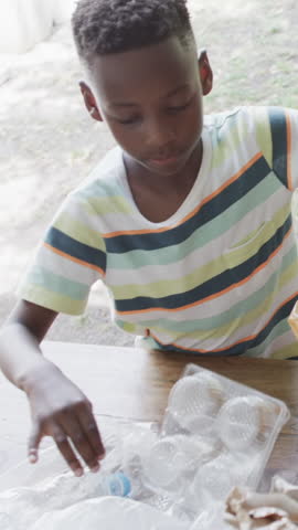 Vertical video: African American boy reaching into bag and unwrapping clear cups on picnic table. Child, outdoor, picnic, packaging, unpacking, handling, vertical video