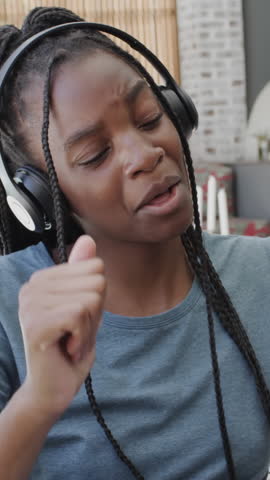 Vertical video: On music start teenage girl with headphones tapping phone, mouthing lyrics at home. Youth, leisure, technology, entertainment, modern, relaxation, vertical video
