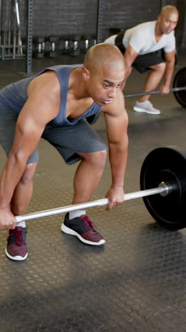 Vertical video: African American males gripping, lifting barbell overhead together at gym for power. Strength, fitness, workout, endurance, athleticism, training, vertical video