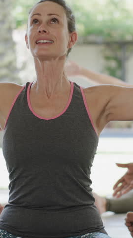 Vertical video: Woman following instructor raising arms upward on outdoor yoga mat stretching. Fitness, wellness, mindfulness, serenity, outdoor, relaxation, vertical video