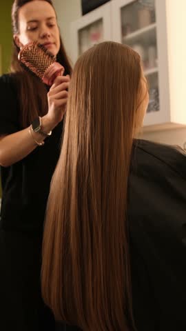 Hairdresser combing and preparing client long hair in salon. Vertical video
