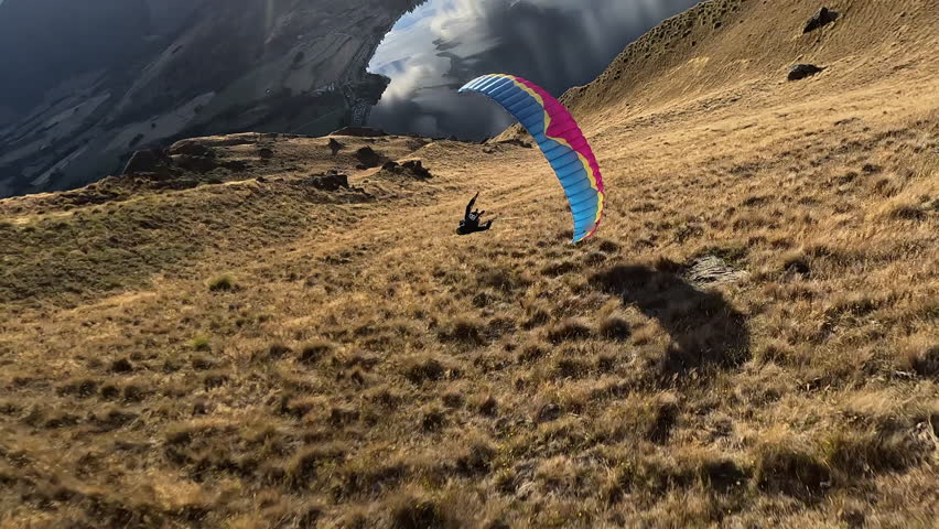 Paraglider point of view flight following another pilot near mountain terrain. Extreme sport action showing speed, skill, and freedom in dramatic outdoor landscape.