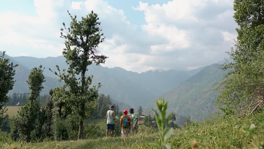 Three young men, a blonde man, a brunette man, and a man wearing a red cap, consulting travel content together near Shangarh, Himachal Pradesh, India. Slow motion.