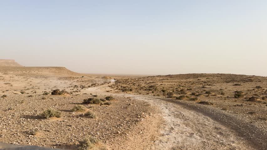 Winding dusty track leads across rocky barren land with low vegetation under hazy sky distant cliffs and endless horizon symbolizing resilience solitude adventure and the raw beauty of wilderness