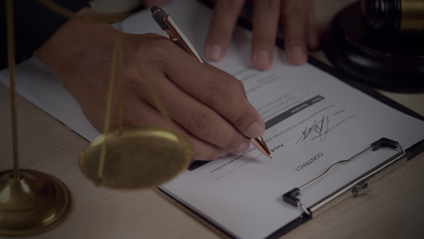 Hand signing a legal business contract with digital data interface showing financial regulation, intellectual property, and compliance analytics. Futuristic legal tech concept.