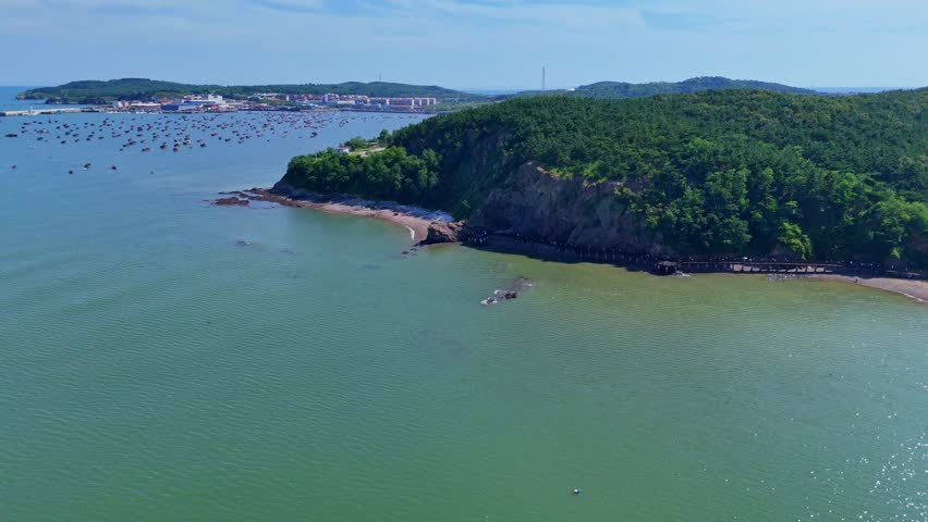 View of the Dalian scenic coast with small fishing boats moored near the rocky shoreline, captured with a dolly-in camera movement. August 26, 2025 - Dalian, China.