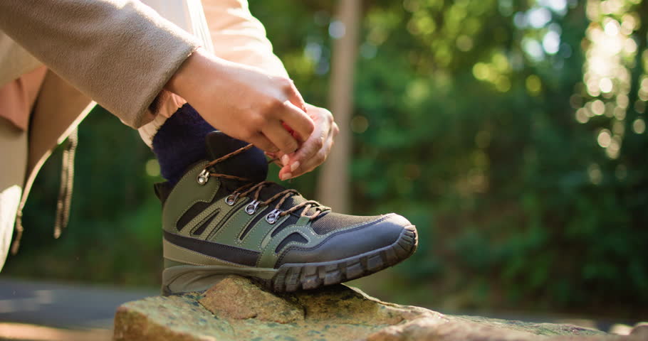 Person, hands and tying with shoes for hiking preparation, walk or outdoor journey in nature. Closeup, hiker or getting ready with tie, laces or boots for trekking adventure or exercise in forest