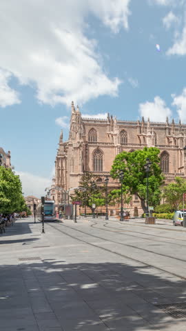 General Archive of the Indies Timelapse hyperlapse in Seville, Spain, housed in the ancient merchants exchange. Tram moving along Avenue de la Constitucion. Blue sky with scattered clouds.